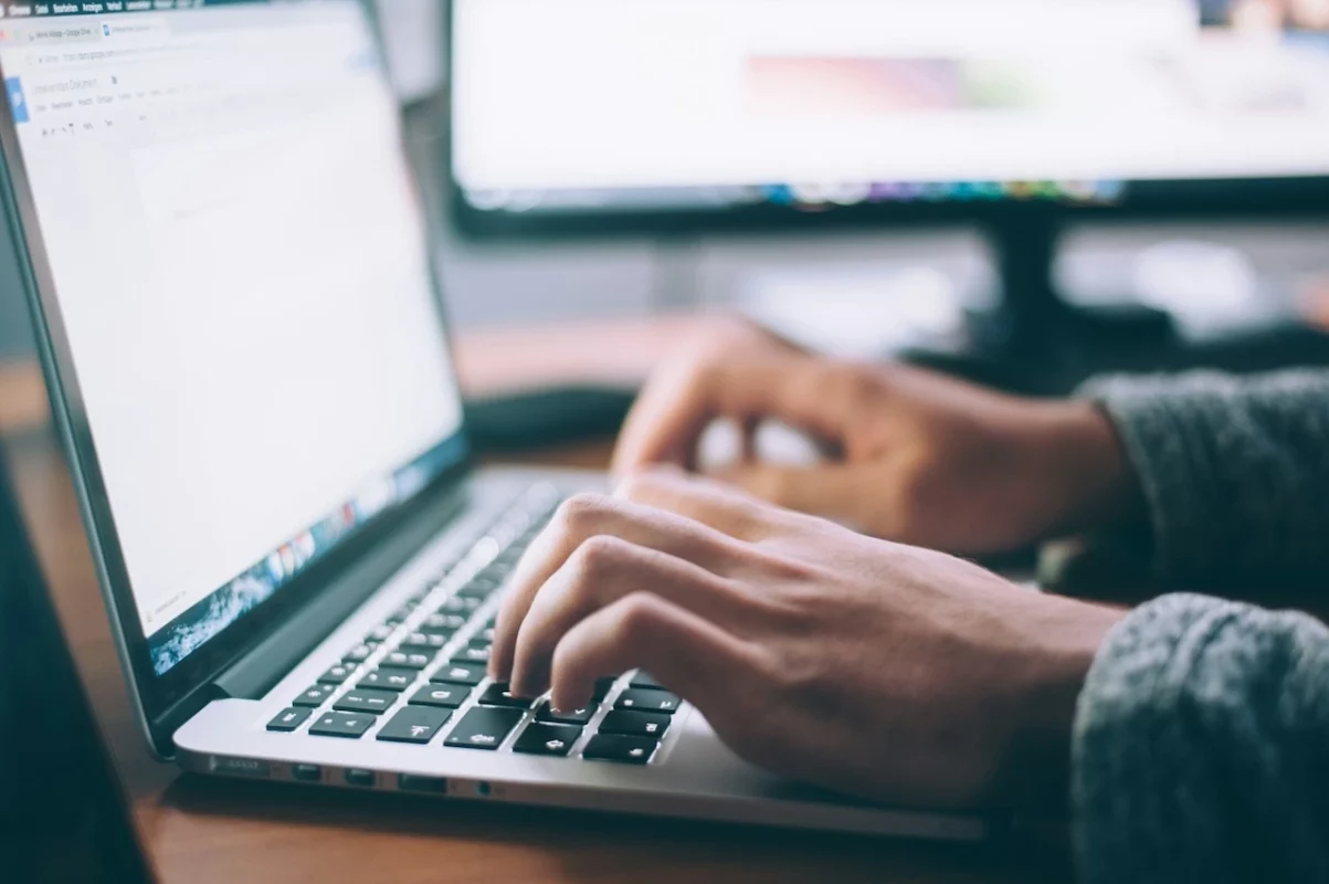 A person typing on a laptop with both hands on the keyboard, while the laptop screen displays a progress of a web design interface in a well-lit workspace.