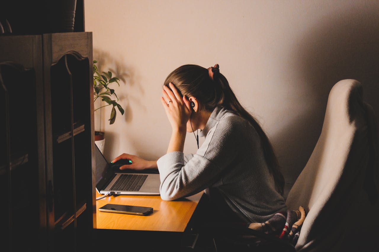 A woman sitting in front of her laptop, holding her head in frustration, expressing the stress of slow internet while trying to work efficiently online.