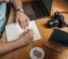 A designer sketching typography ideas in a notebook next to a laptop and camera, reflecting a creative workspace.